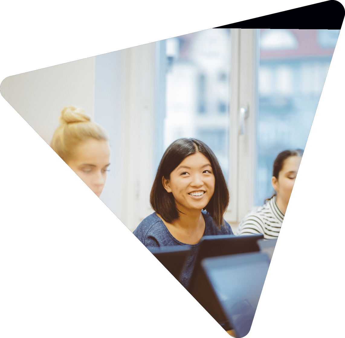 Female students learning computer programming. Focus on asian woman smiling and looking at instructor.