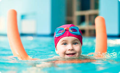 Happy little girl learning to swim with pool noodle