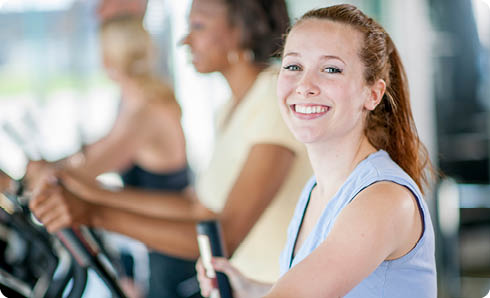 A young woman is smiling and working out on the treadmill at the gym.
