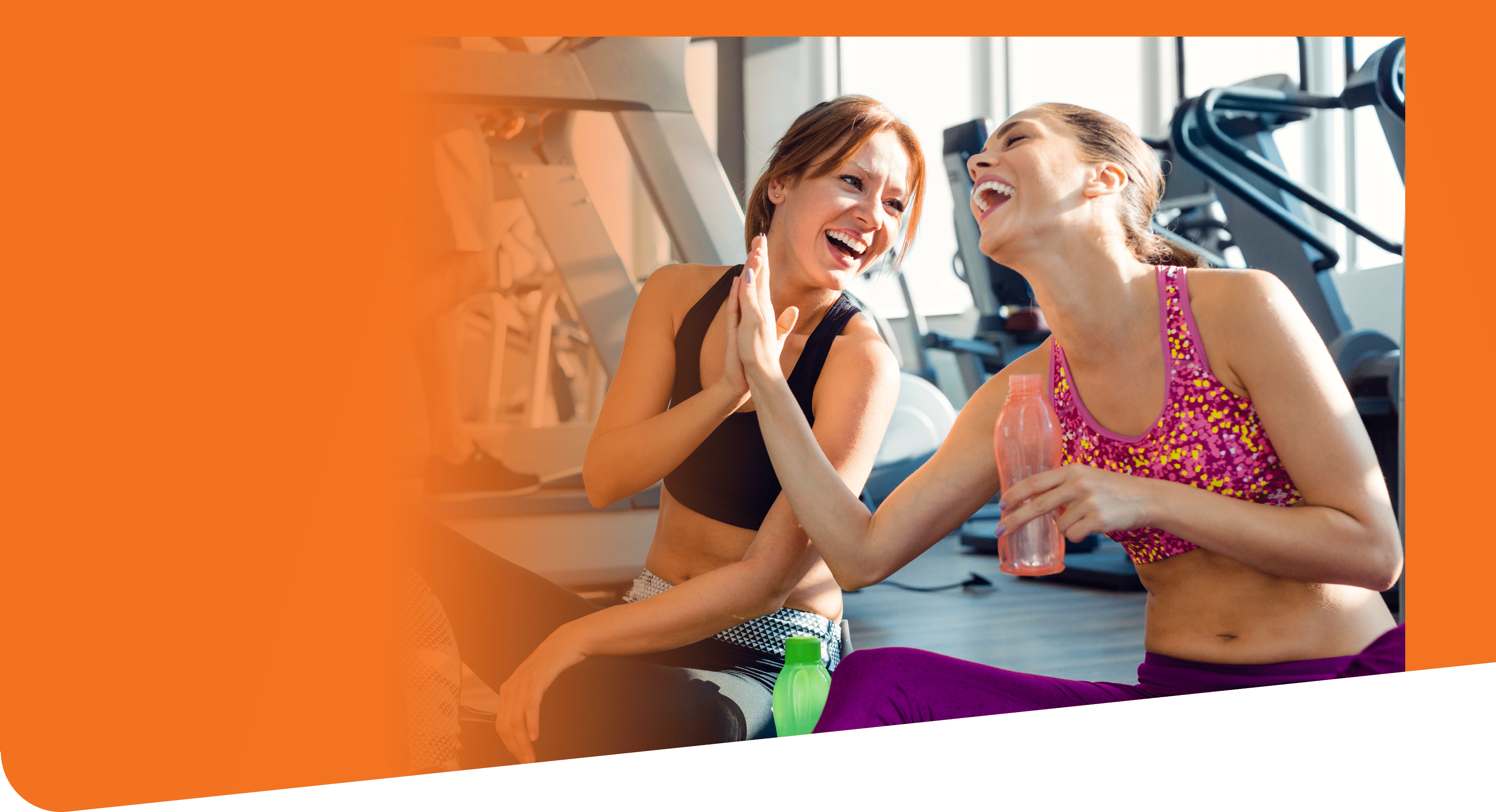 Young female friends sitting on exercise mat in the gym and giving high five after training.