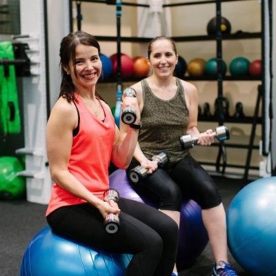 Two people smiling and using hand weights at the gym