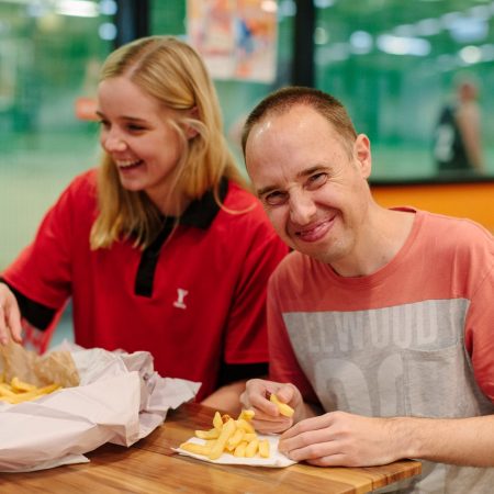 Two people at a table, including a YMCA staff member, smiling and eating hot chips