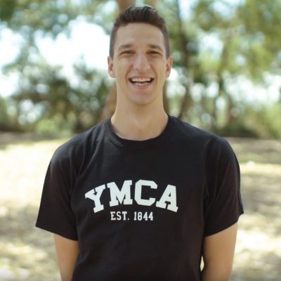 Outdoor photo of Andrew smiling and wearing YMCA t-shirt