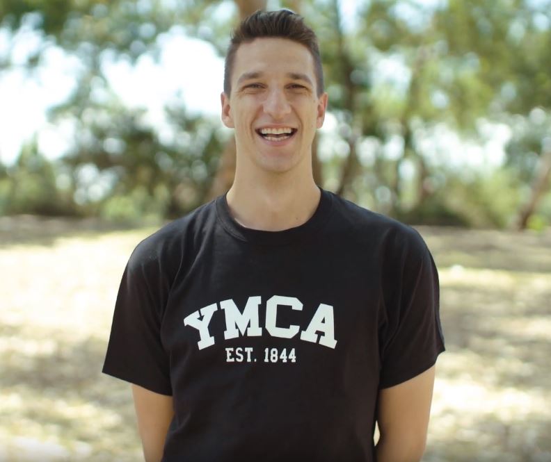 Outdoor photo of Andrew smiling and wearing YMCA t-shirt