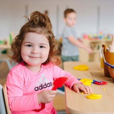 Toddler smiling at the camera and sitting at a size appropriate table, playing with play dough