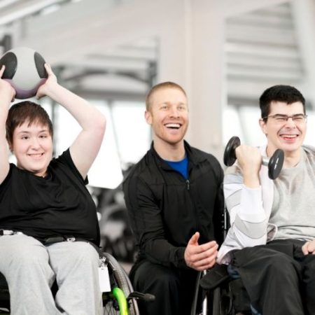 Two people in wheelchairs and one kneeling down, laughing and engaging in activities
