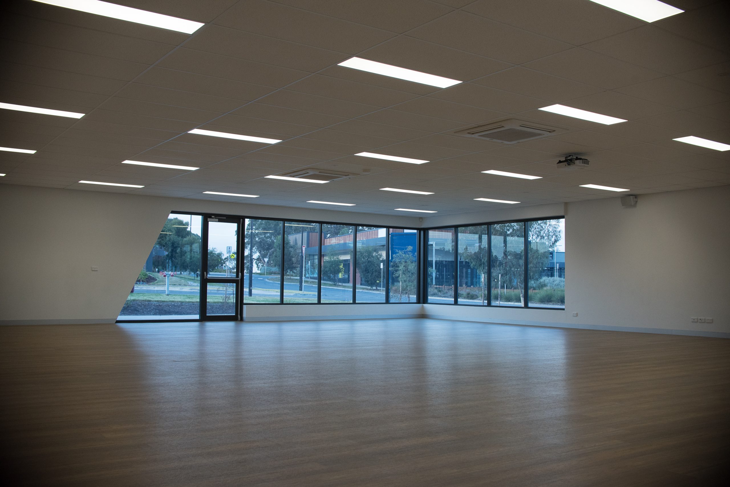 Very large empty room with wooden floors and lots of natural light. Two walls include a lot of windows and a glass door onto the garden and street.